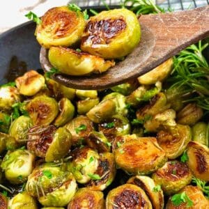 Three sauteed brussels sprouts on a wood spoon over a pan of finished recipe.