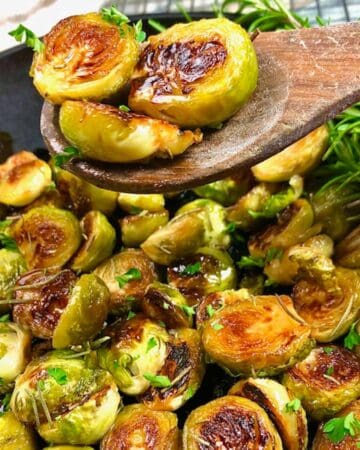 Three sauteed brussels sprouts on a wood spoon over a pan of finished recipe.
