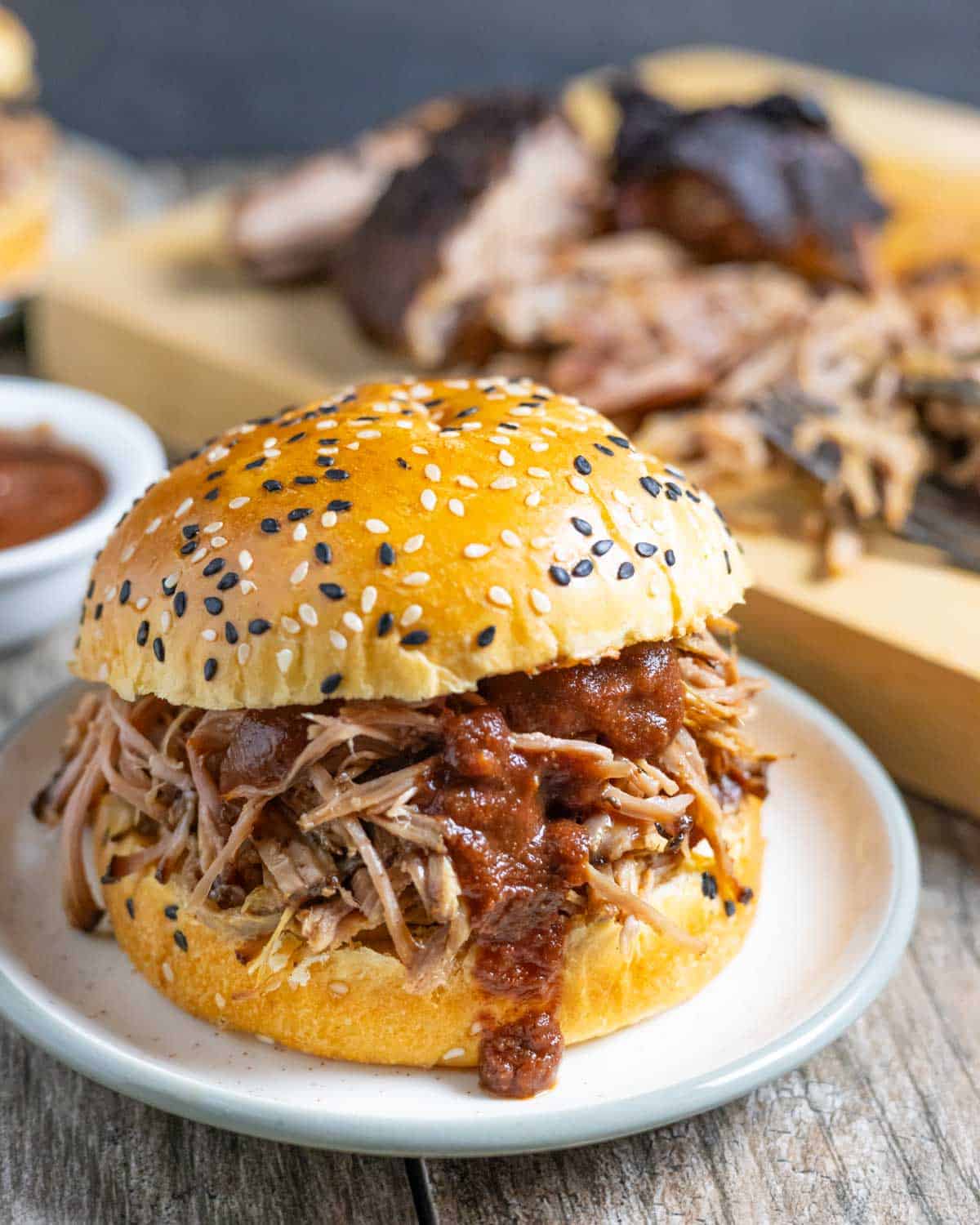 Pulled pork on a sesame seed bun with homemade no-cook bbq sauce dripping over the pork and bottom bun.