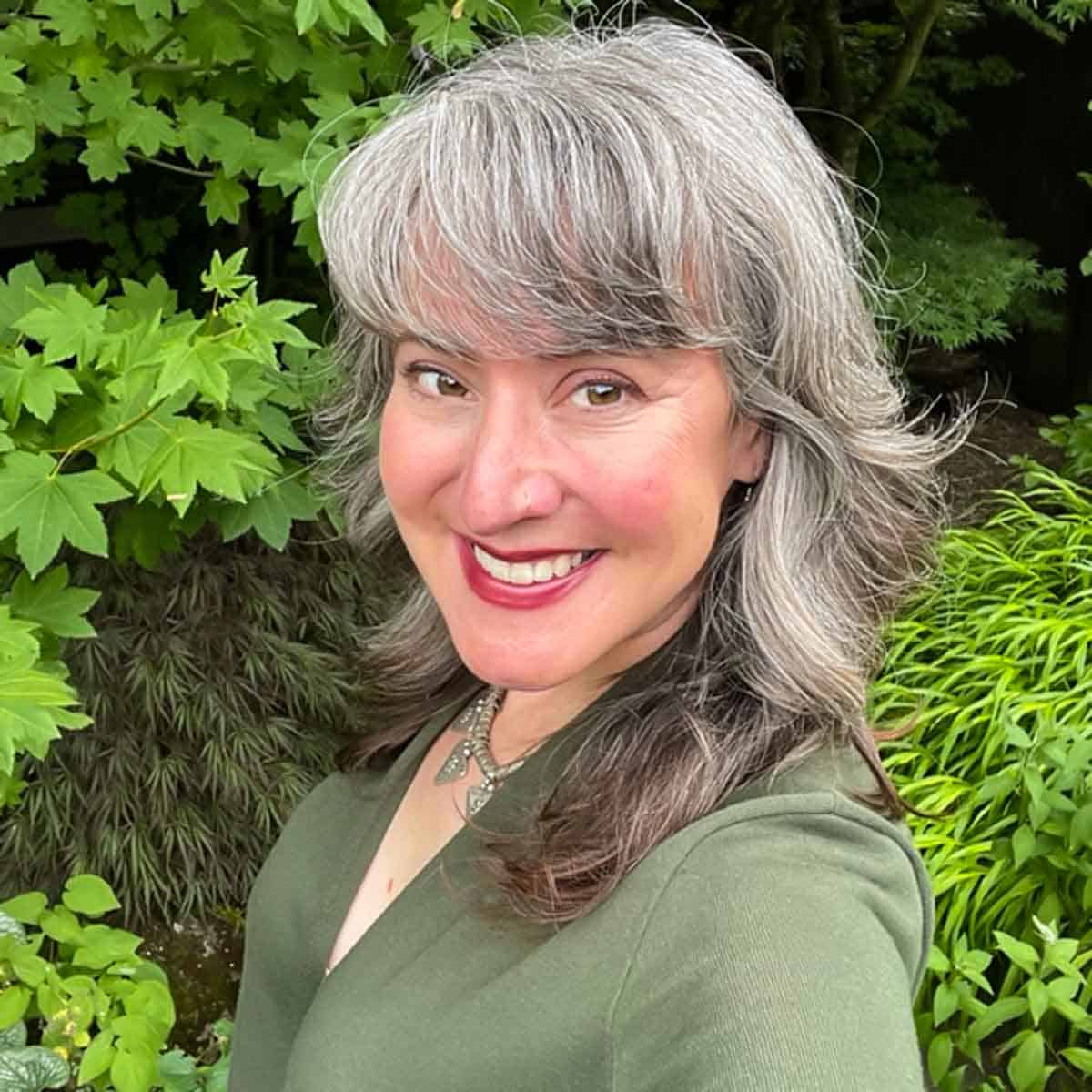 Author headshot outside in front of green maples and grasses.