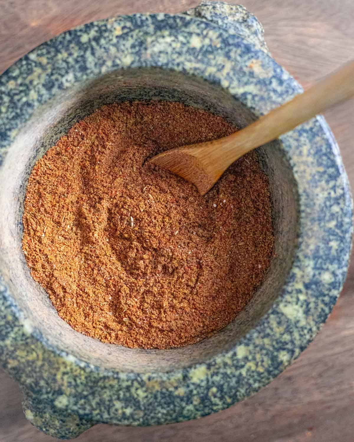 Powdered pulled pork rub in a granite mortar with a small wood spoon in the bowl.