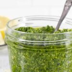 Side of small glass mason jar with pesto and a spoon in it.