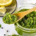 Jar of basil pesto with small wood spoonful laying across the top.