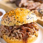 Pulled pork on a sesame seed bun with homemade no-cook bbq sauce dripping over the pork and bottom bun.
