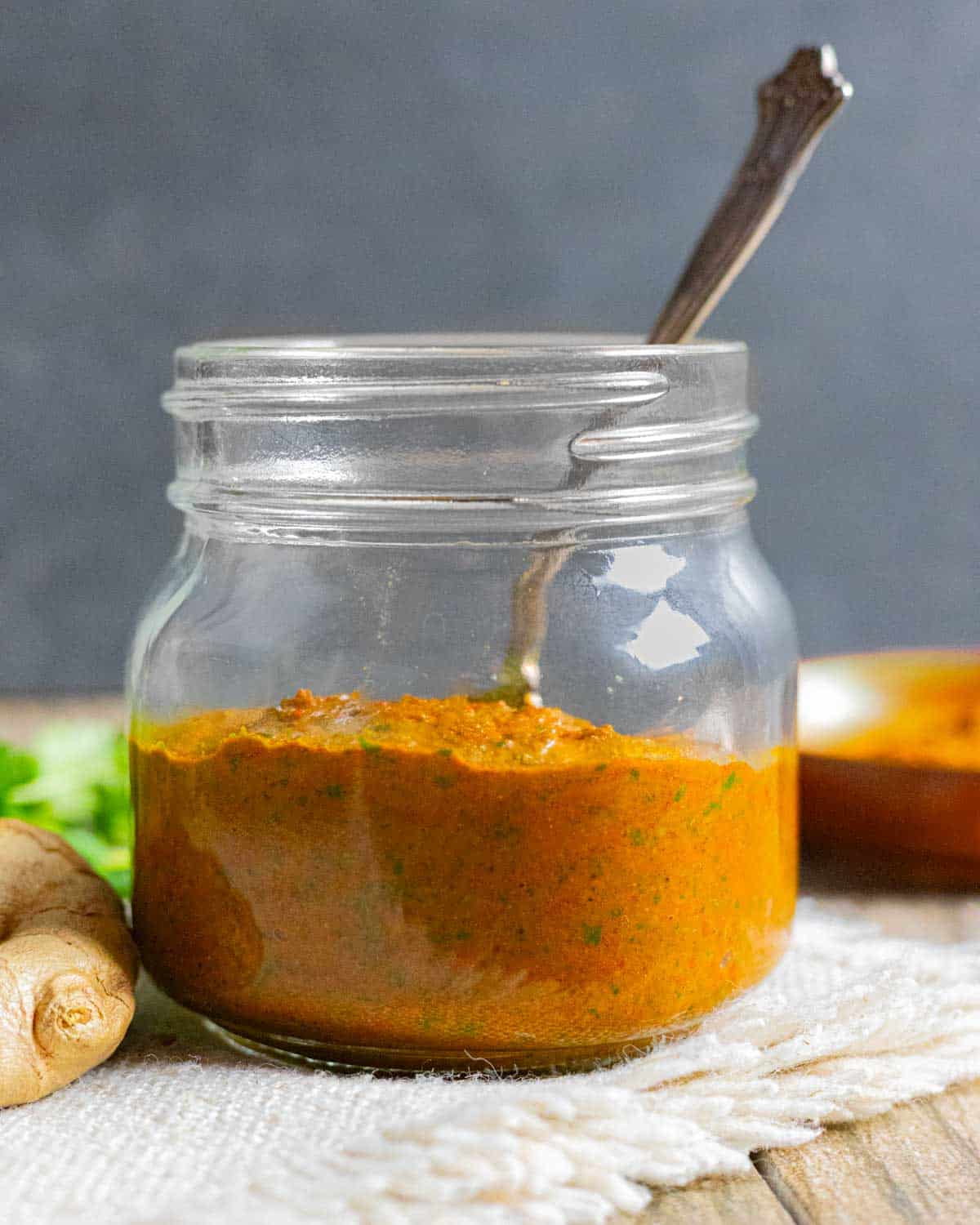 Small glass jar of tikka masala paste with a spoon in it and ginger root next to the jar.