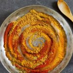 Powdered ingredients for tikka masala spice mix swirled into a spiral of various colors in a pewter dish.