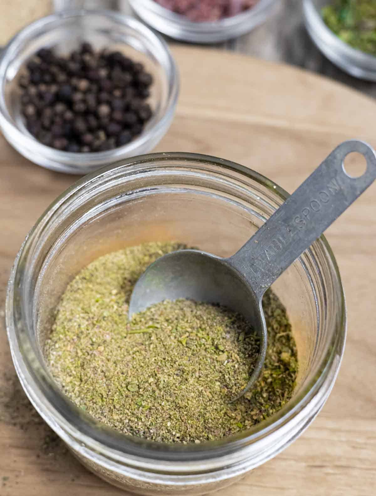 Glass jar of powdered all purpose seasoning with a measuring spoon inside.