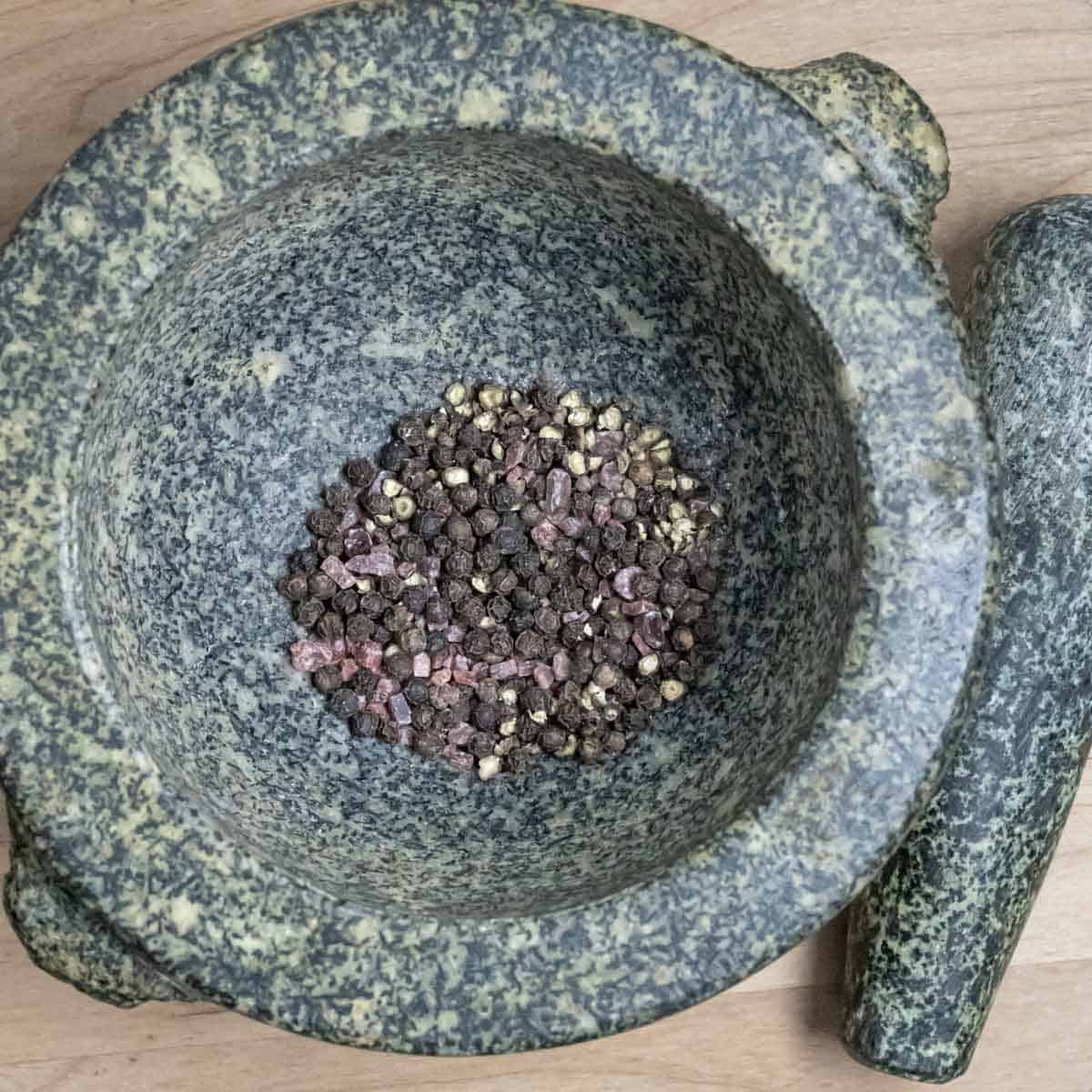 Peppercorns and coarse salt in a granite mortar with a pestle on the side.