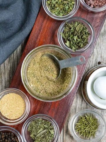 All purpose seasoning in a glass jar surrounded by small bowls of spices.