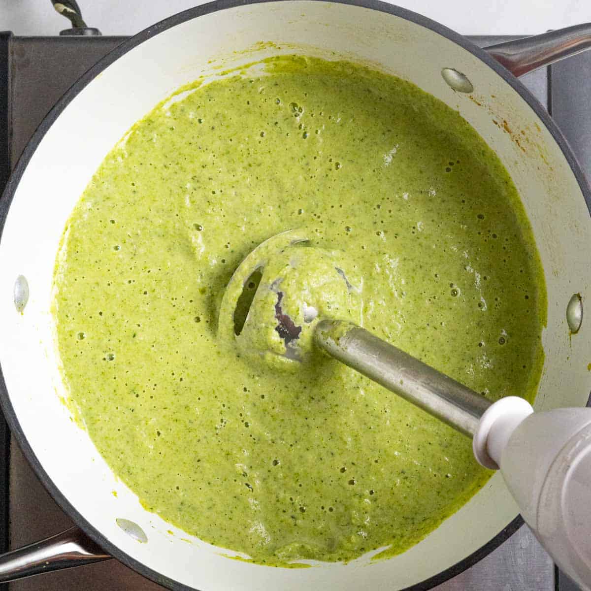 Immersion blender in pot of blended broccoli almond soup.