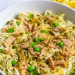 Tuna with noodles, pesto topped with peas and basil leaves in a white bowl.