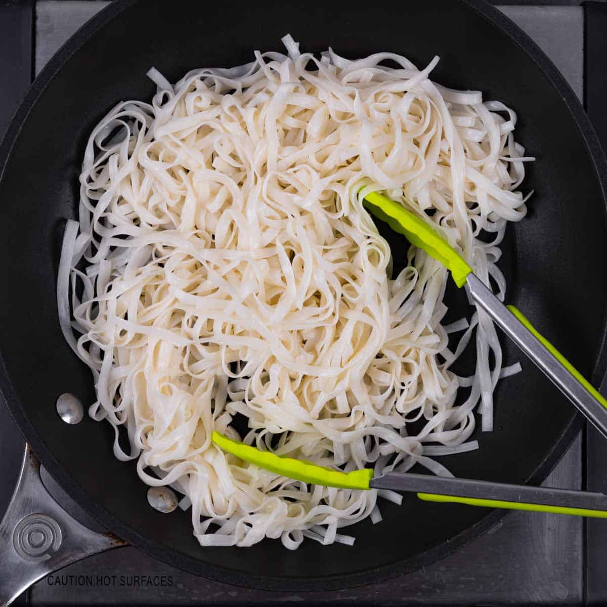 Shirataki noodles in a skillet with tongs.