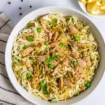 Pasta with tuna and pesto in a bowl topped with a few peas and basil leaves.