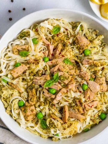 Pasta with tuna and pesto in a bowl topped with a few peas and basil leaves.