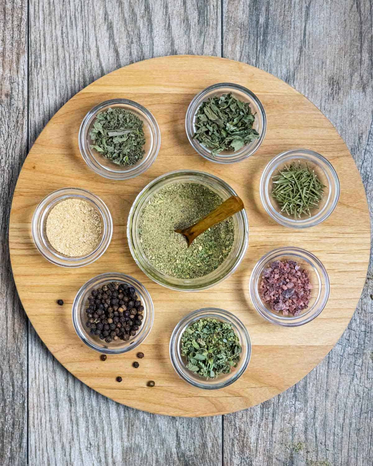 Small glass bowls with spices on a round board with a jar of spice blend in the center.