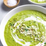 Creamy broccoli soup in a bowl topped with sour cream and sprinkled with herbs and spices.