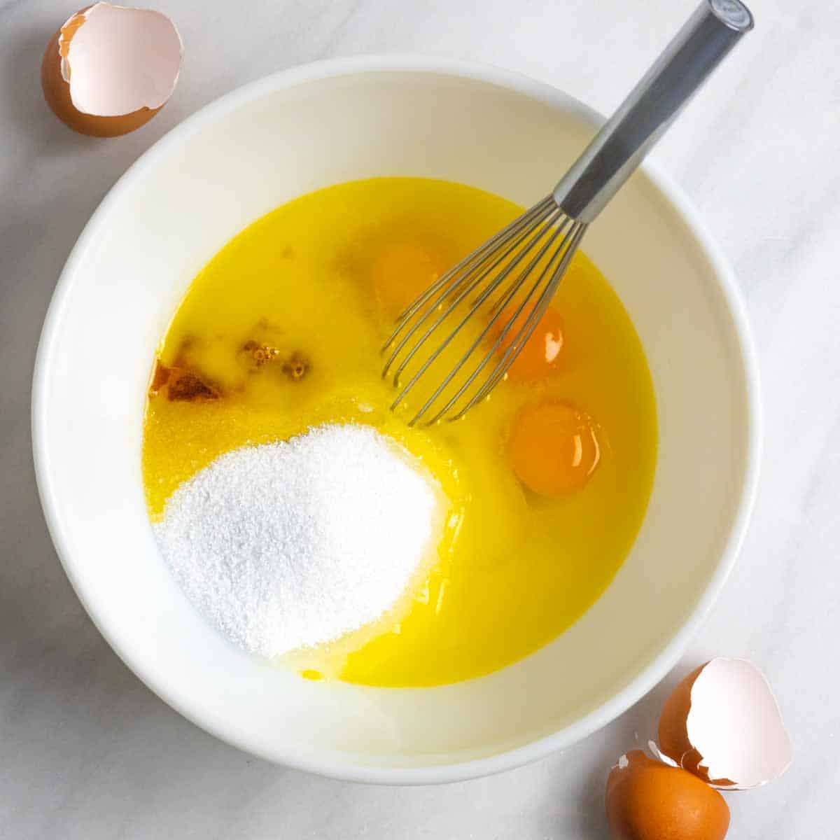 Sweetener with eggs and wet ingredients unmixed in a white bowl with a whisk inside it.