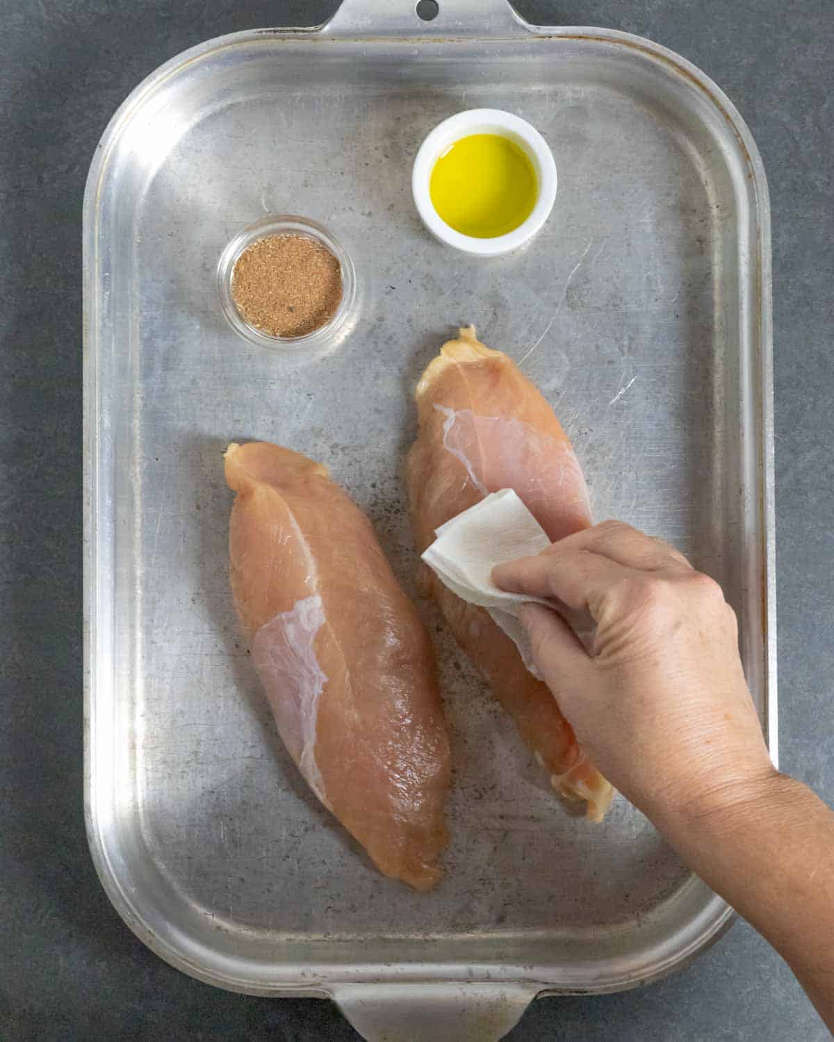 Tenderloins on a steel tray being pat dry with paper towel.