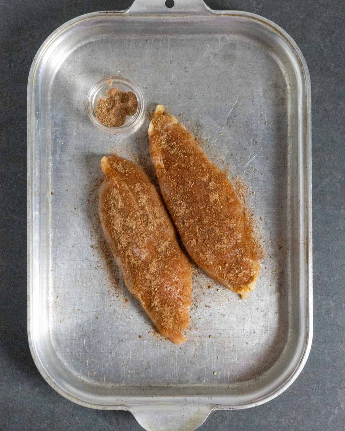 Turkey breast tenders seasoned with rub on a steel tray.