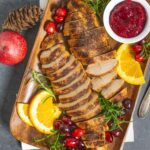 Platter of sliced air fryer turkey tenderloins with cranberries, jam, and herbs.