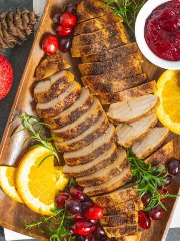 Platter of sliced air fryer turkey tenderloins with cranberries, jam, and herbs.