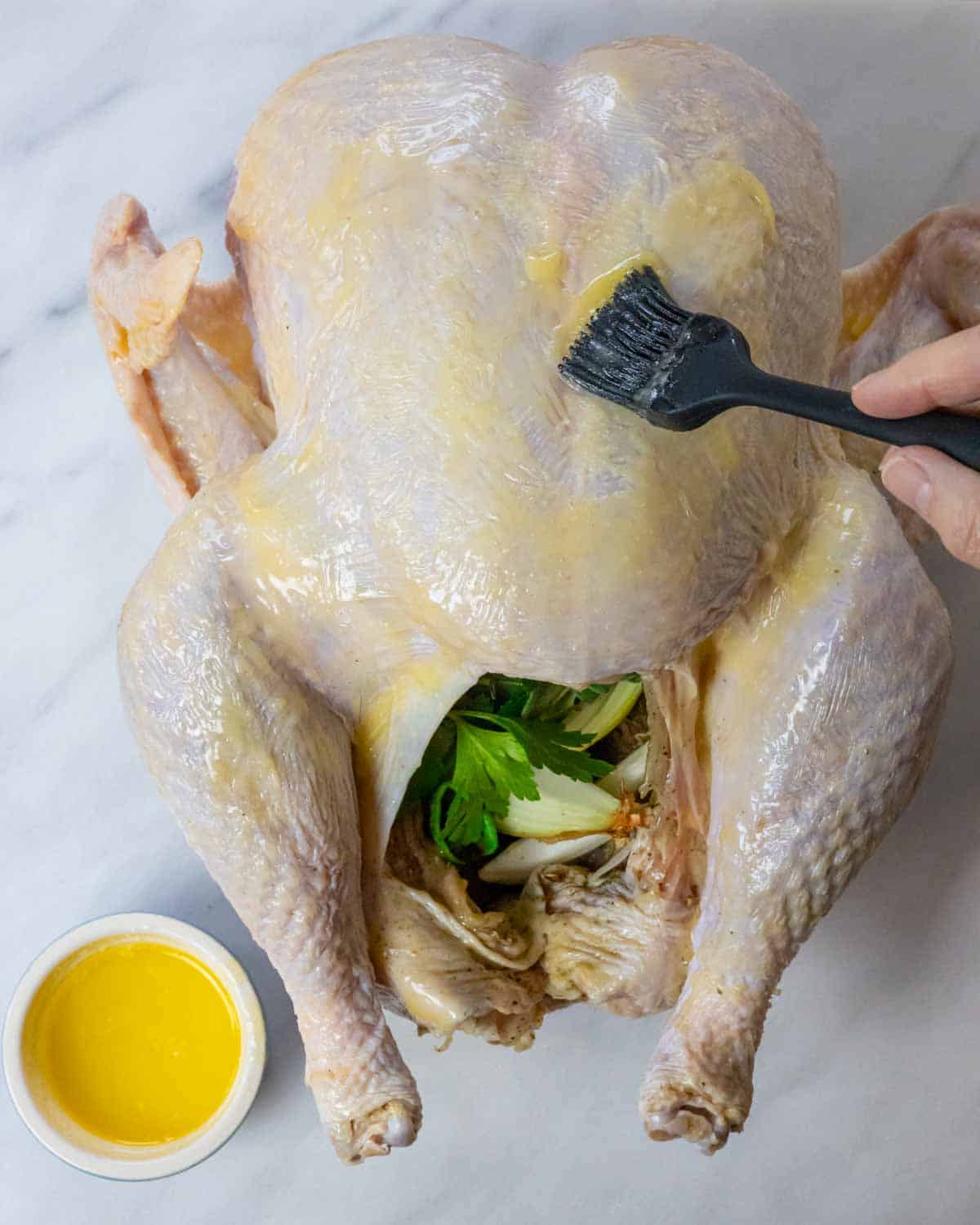 Stuffed raw turkey being basted with butter.