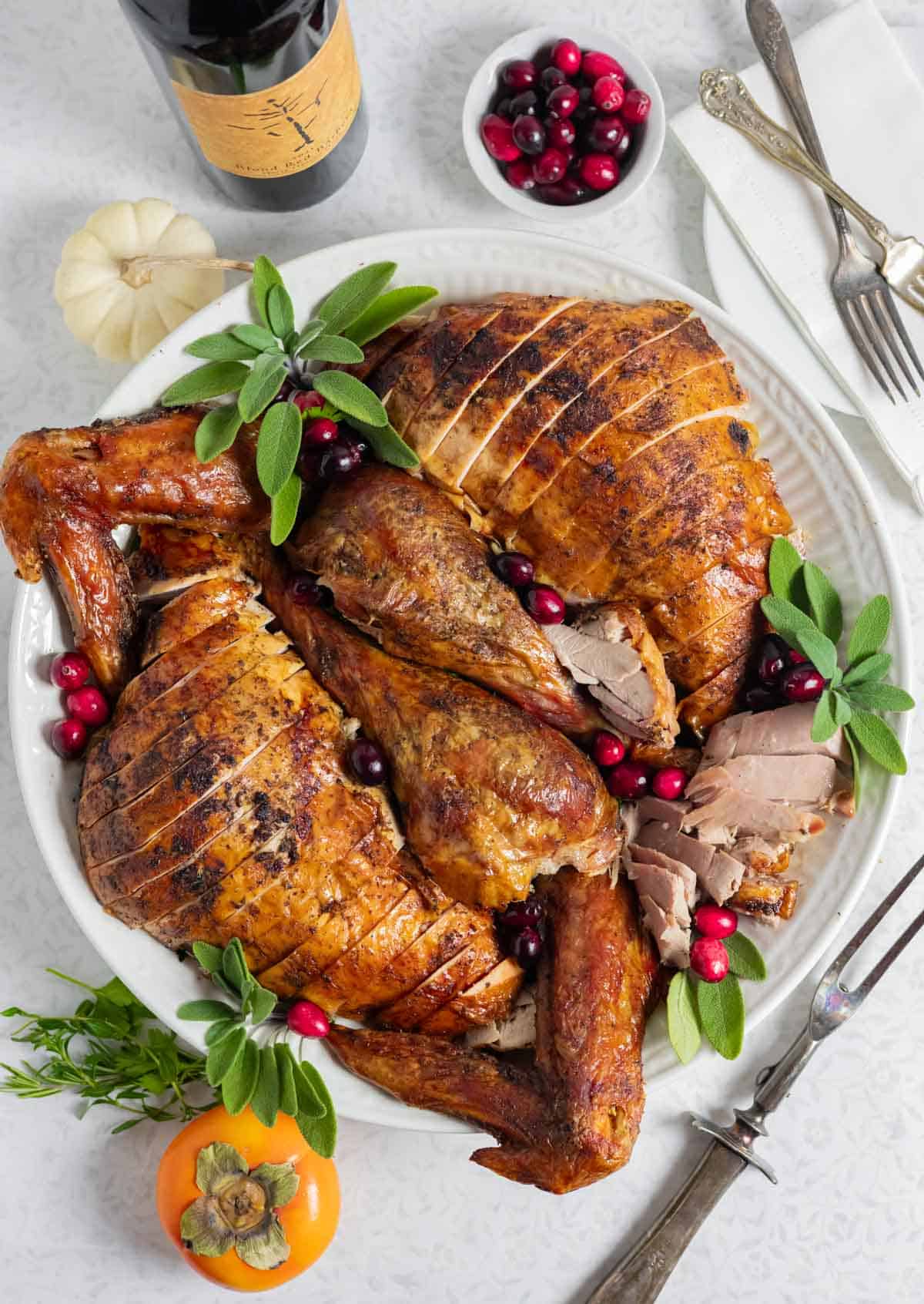 Crispy convection turkey carved on a platter with fresh sage and cranberries.