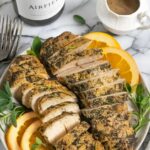 Two sliced turkey tenderloins on a plate garnished with orange slices and herbs.