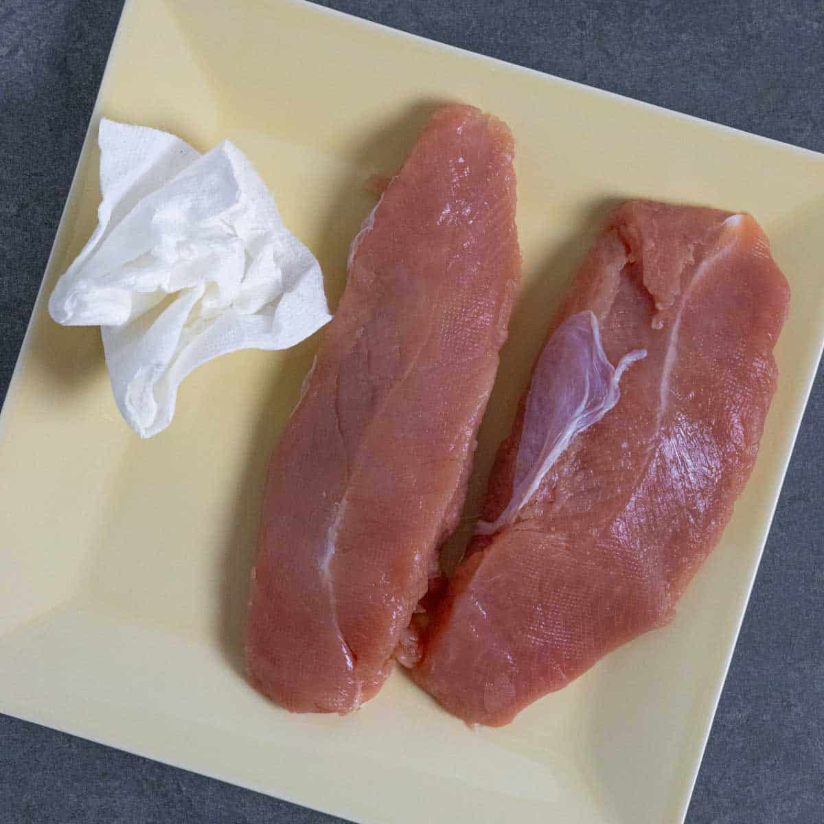 Turkey tenderloins on a plate with a paper towel to remove extra moisture.