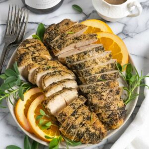 Plate of crockpot turkey tenders sliced with herbs and orange slices