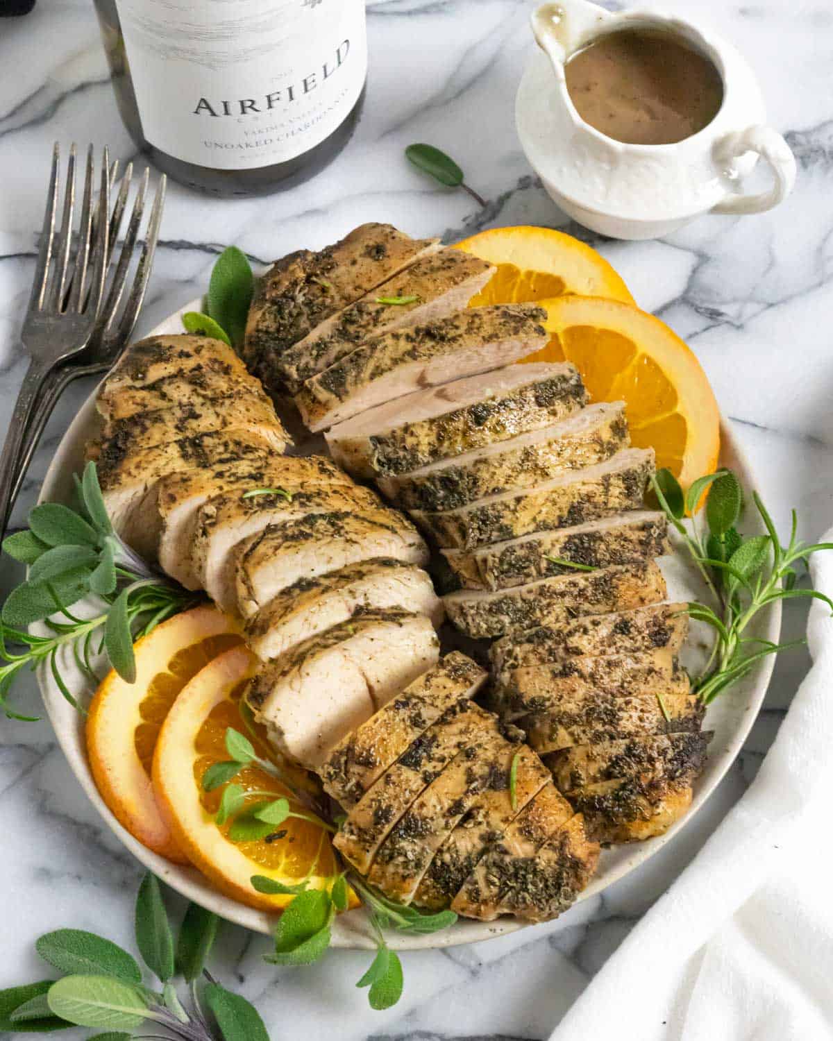 Two sliced turkey tenderloins on a plate garnished with orange slices and herbs.