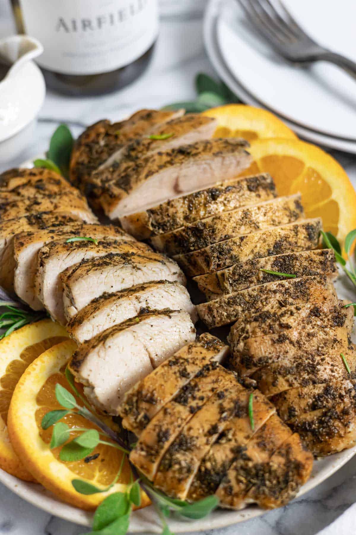 Slow cooker seasoned turkey breast tenders sliced on a plate with herbs and orange slices.