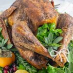 Crisp, golden whole turkey on a platter with herbs in the cavity and platter.