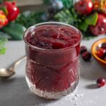 Fancy jar of bright red cranberry jam with festive greens behind.