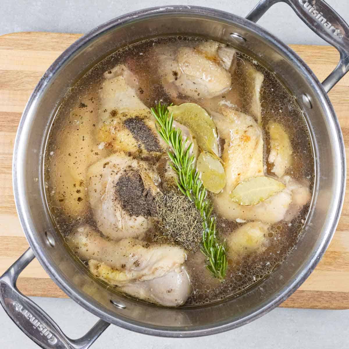 Chicken, herbs and broth in soup pot to simmer for Spanish soup.