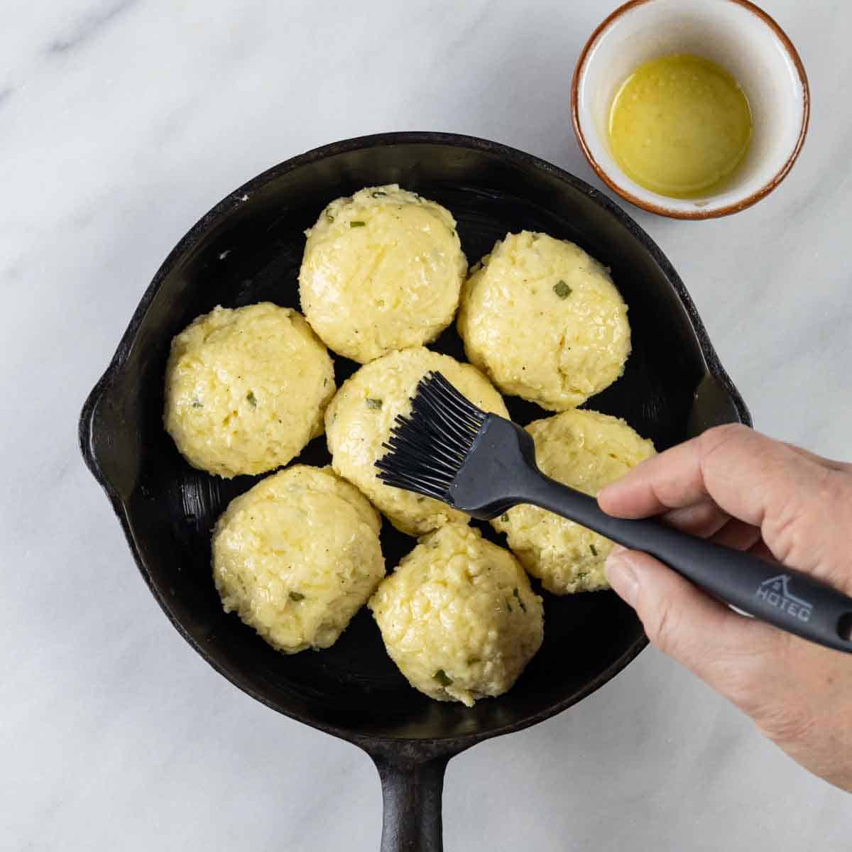 Balls of dough in a cast iron skillet being brushed with melted butter.