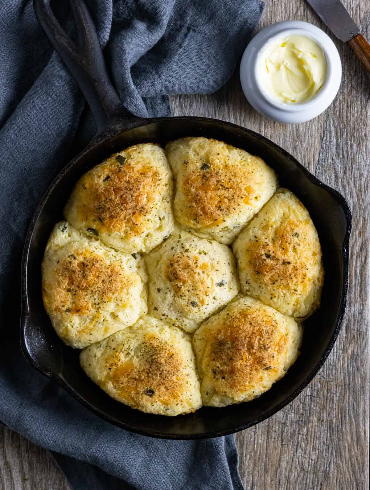 Seven golden rolls baked in a small cast iron skillet topped with herbs.