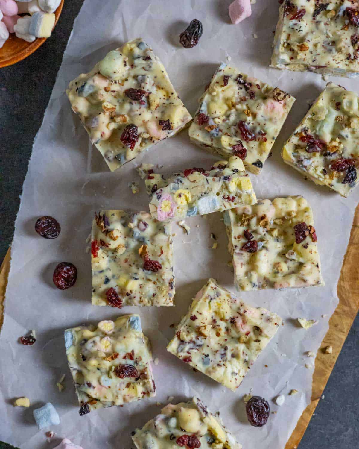 Squares of rocky road topped with dried cranberries on parchment.