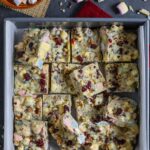 Squares of cranberry sprinkled white chocolate rocky road placed loosly in a baking pan.