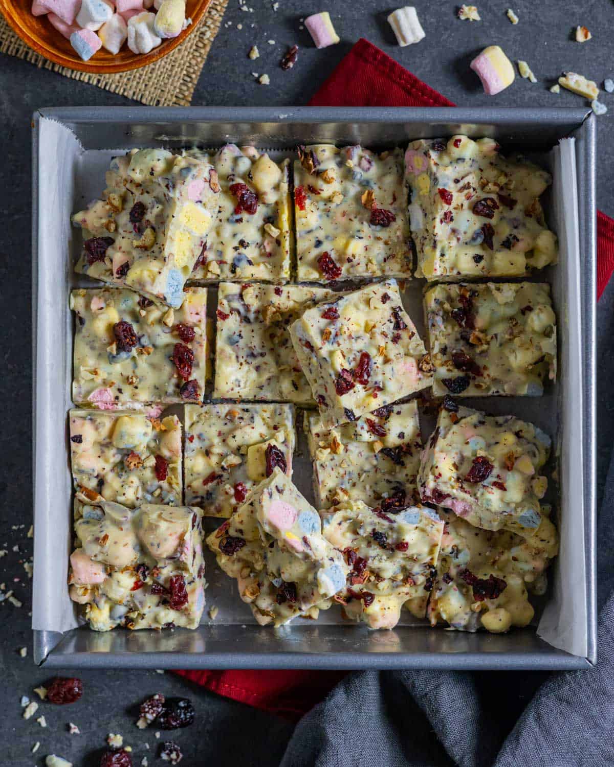 Squares of cranberry sprinkled white chocolate rocky road placed loosly in a baking pan.