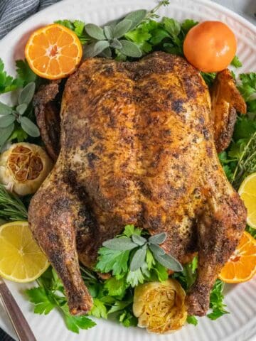 Convection roasted whole chicken on a platter with herbs and citrus garnish.
