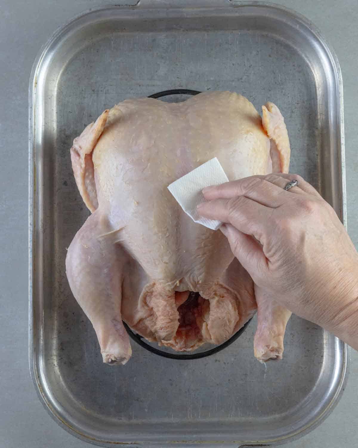 Removing excess moisture from whole raw chicken with a paper towel.