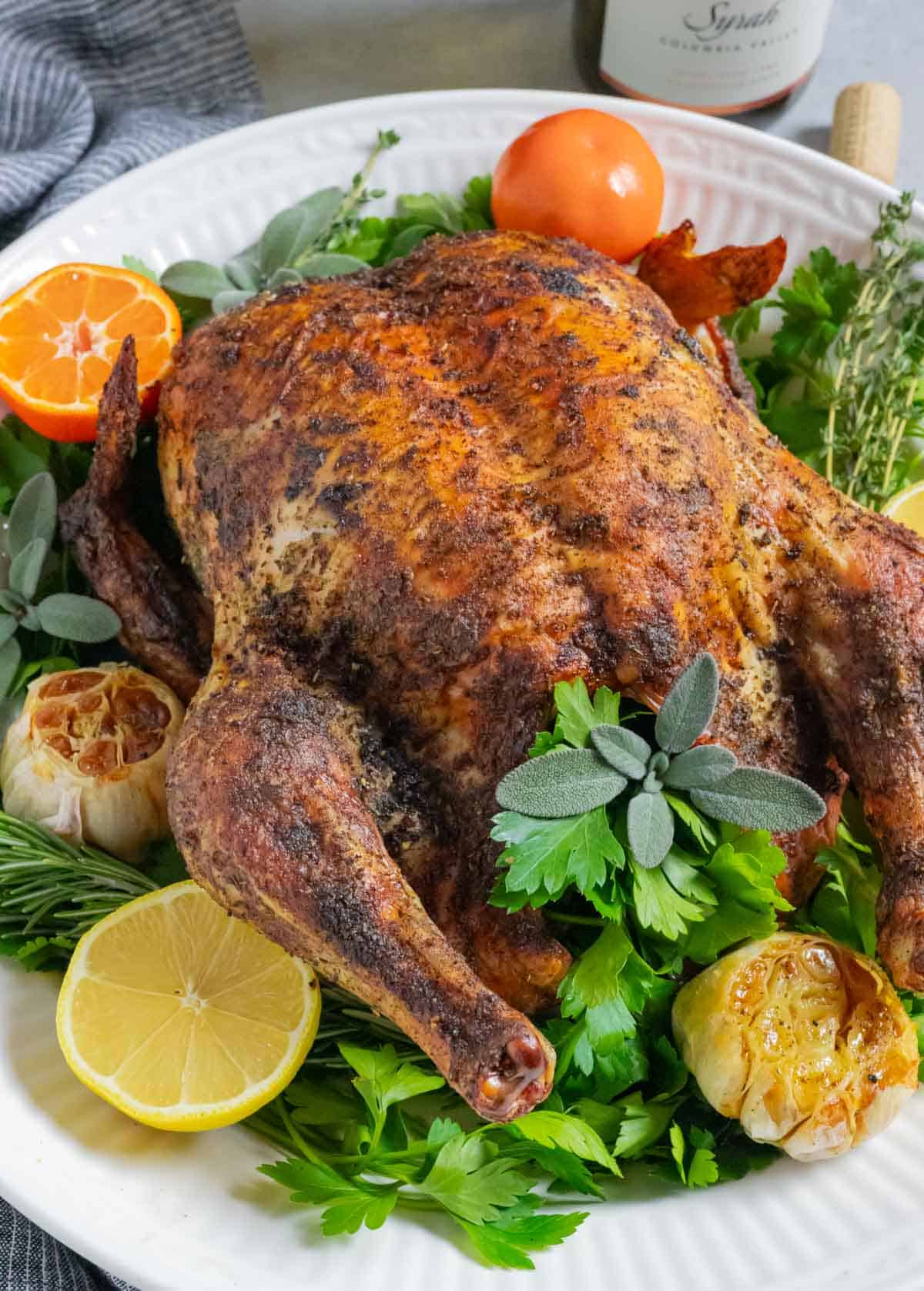 Crispy skninned roasted whole chicken on a platter with roasted garlic, citrus and herbs.