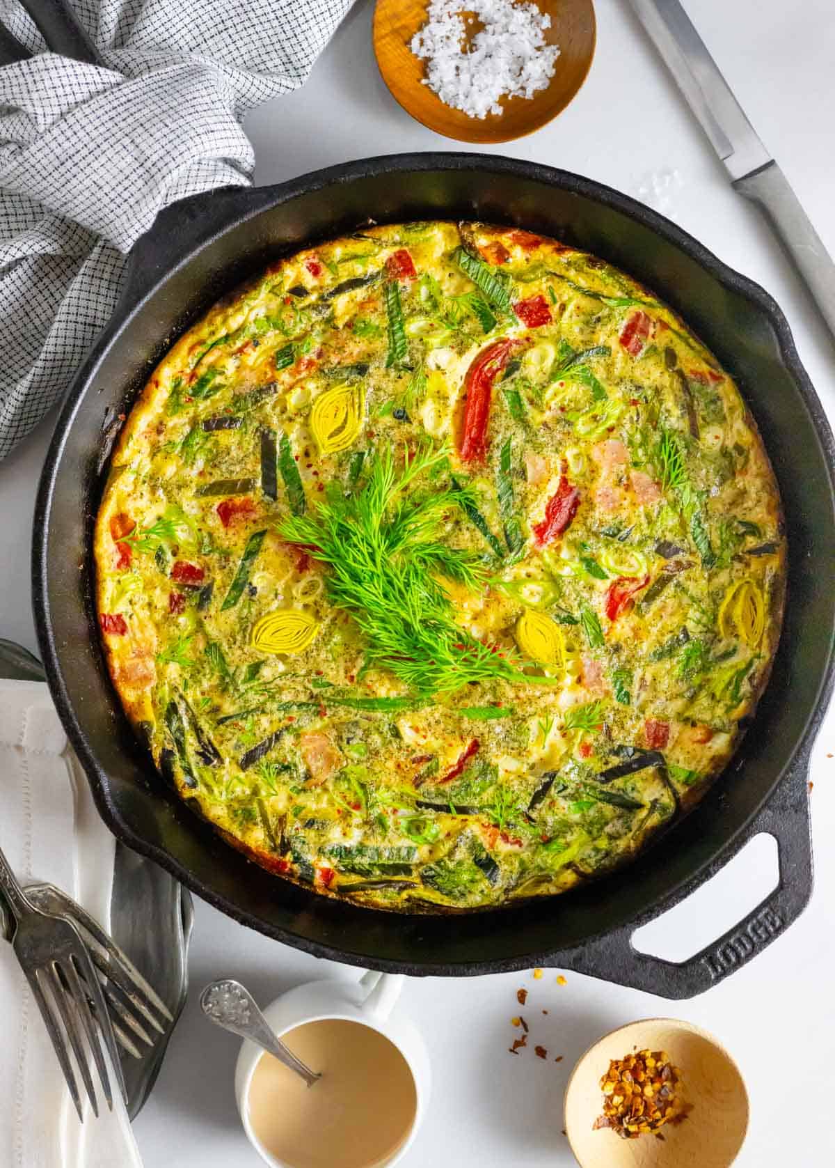 Baked frittata garnished with fresh dill in a cast iron skillet.