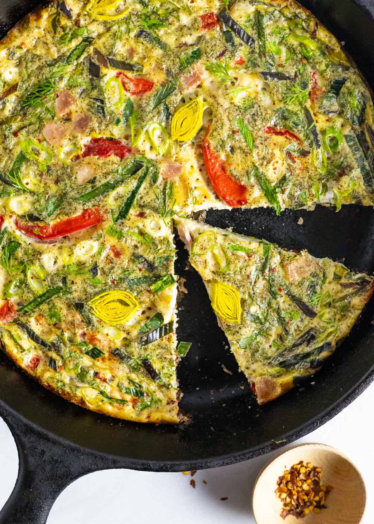 Baked dairty-free frittata in a cast iron pan with one slice separated.