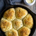 Seven golden rolls baked in a small cast iron skillet topped with herbs.