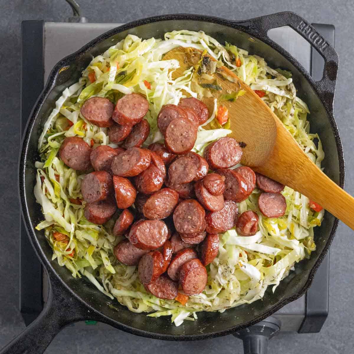 Adding browned sausage back to skillet of cabbage and vegetables and simmer.
