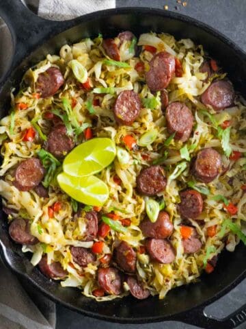 Keto cabbage and sausage fried with chopped vegetables in a cast iron skillet.