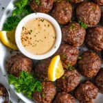 Plate of over a dozen corned beef meatbals with herbs, lemon wedges and horseradish mustard sauce.