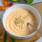 White bowl of dairy-free Thousand Island dressing on a wood board with herbs.